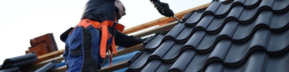 A Man is Working on a Roof With a Drill — East Coast Roof Tiling Services in Kuluin, QLD