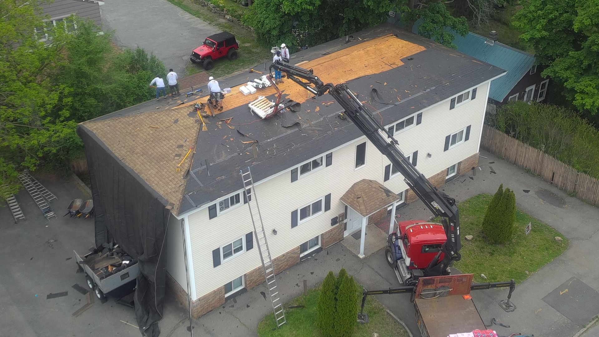 Aerial view of roof repair on a two-story house, with workers, debris, and a red truck parked below