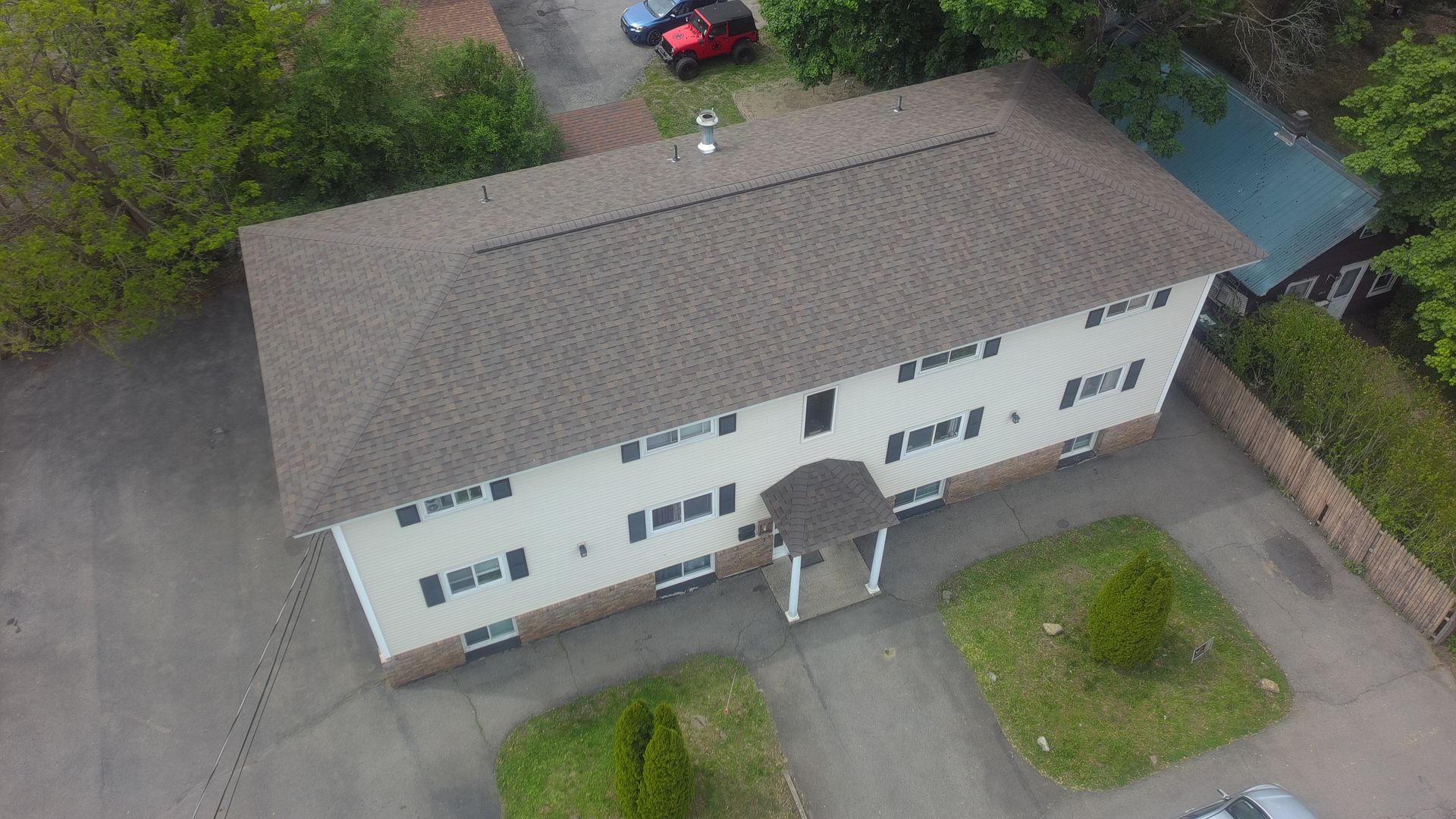 Aerial view of a white apartment building with a gray roof, parked cars, and a small lawn.