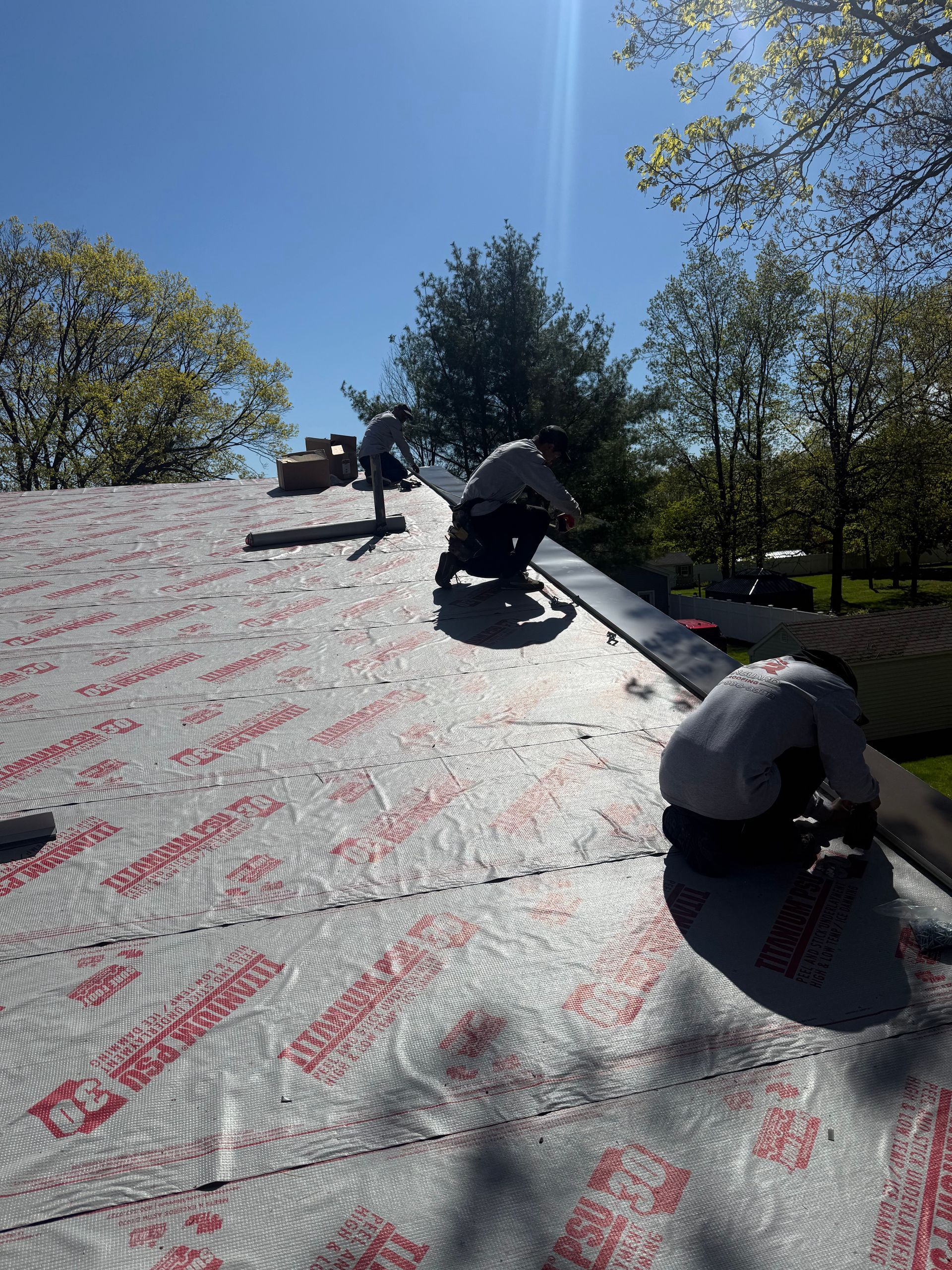 Workers installing roofing underlayment on a steep roof in bright sunlight