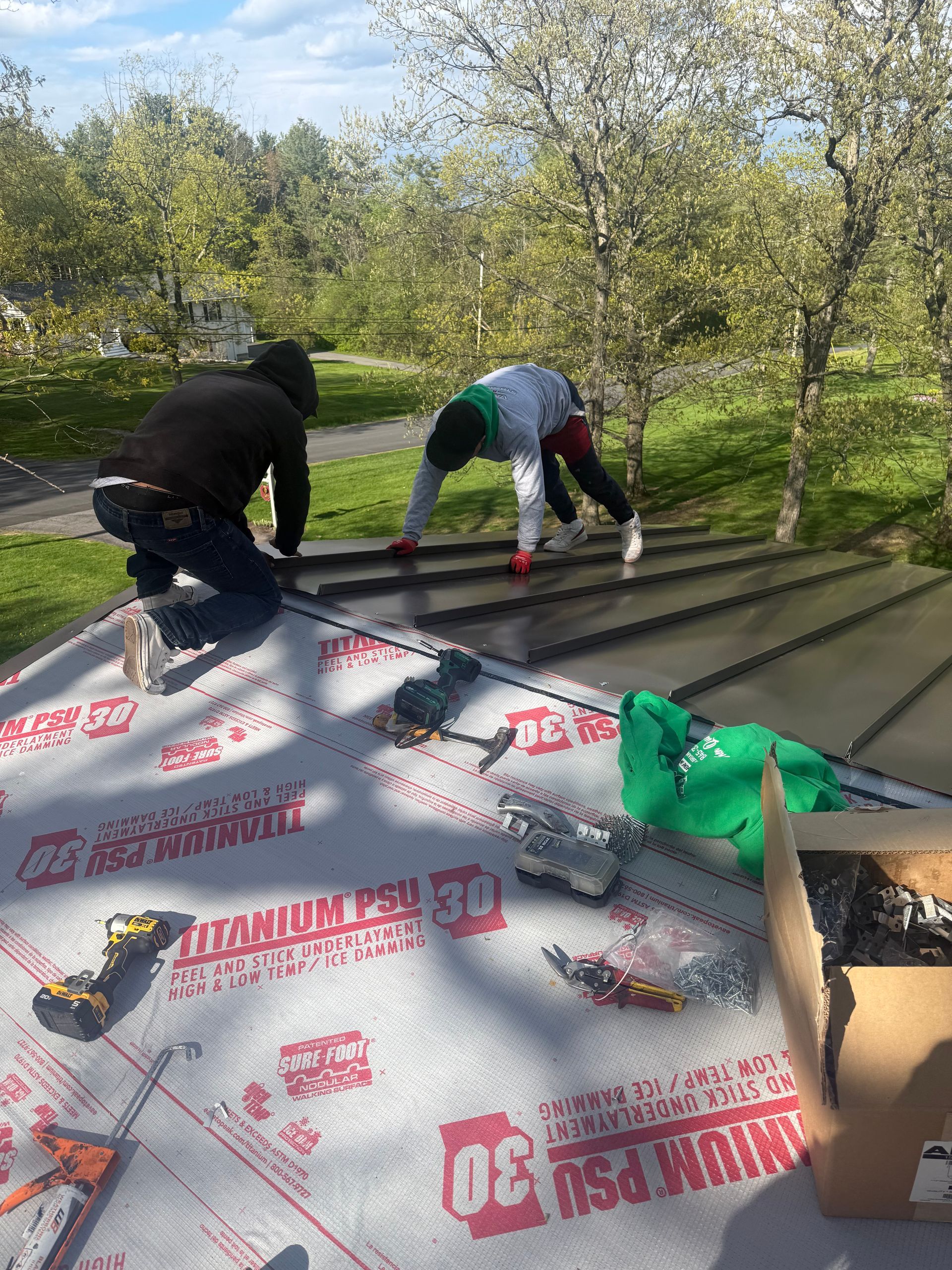 Two workers installing roofing underlayment on a sloped roof in a sunny orchard setting