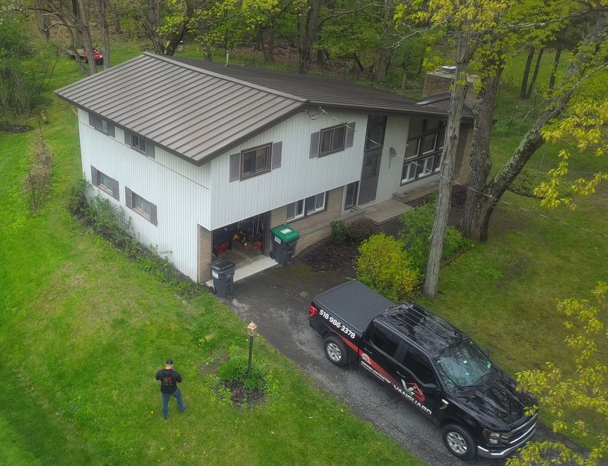 Aerial view of a white house in a wooded yard with a black pickup truck and one person standing outside
