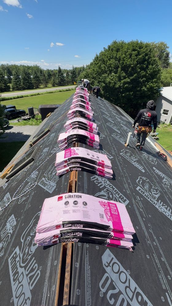 Workers installing pink roofing underlayment on a long rooftop on a sunny day