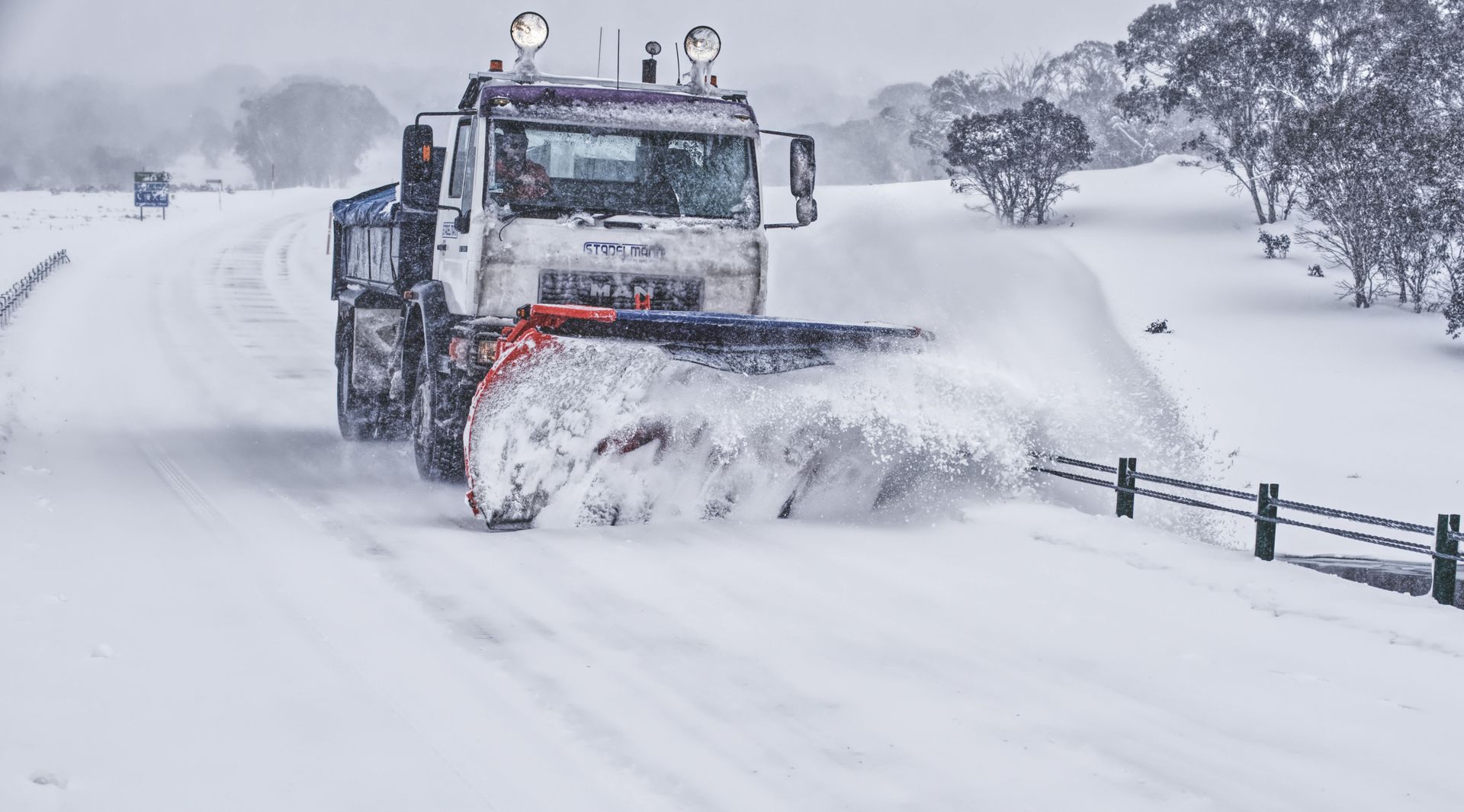 Snowplow clears a snowy road in a mountainous area.