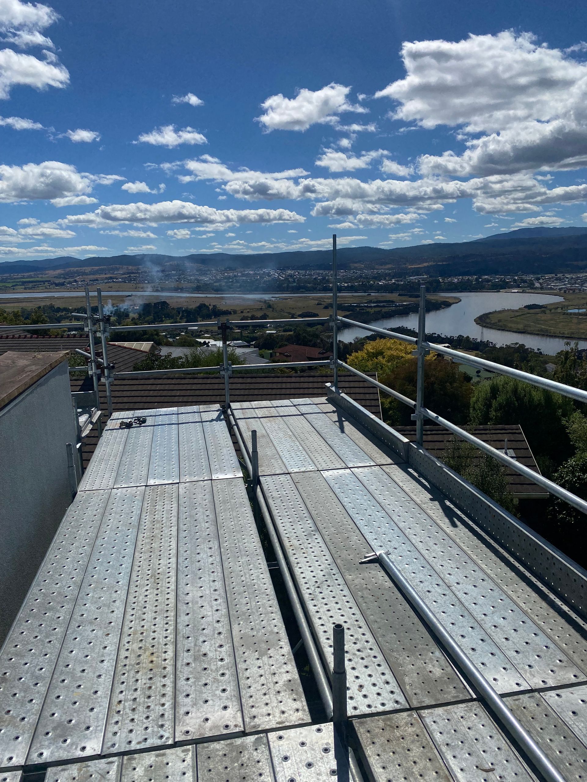 Scaffolded rooftop overlooking a river, city skyline, and blue sky with clouds