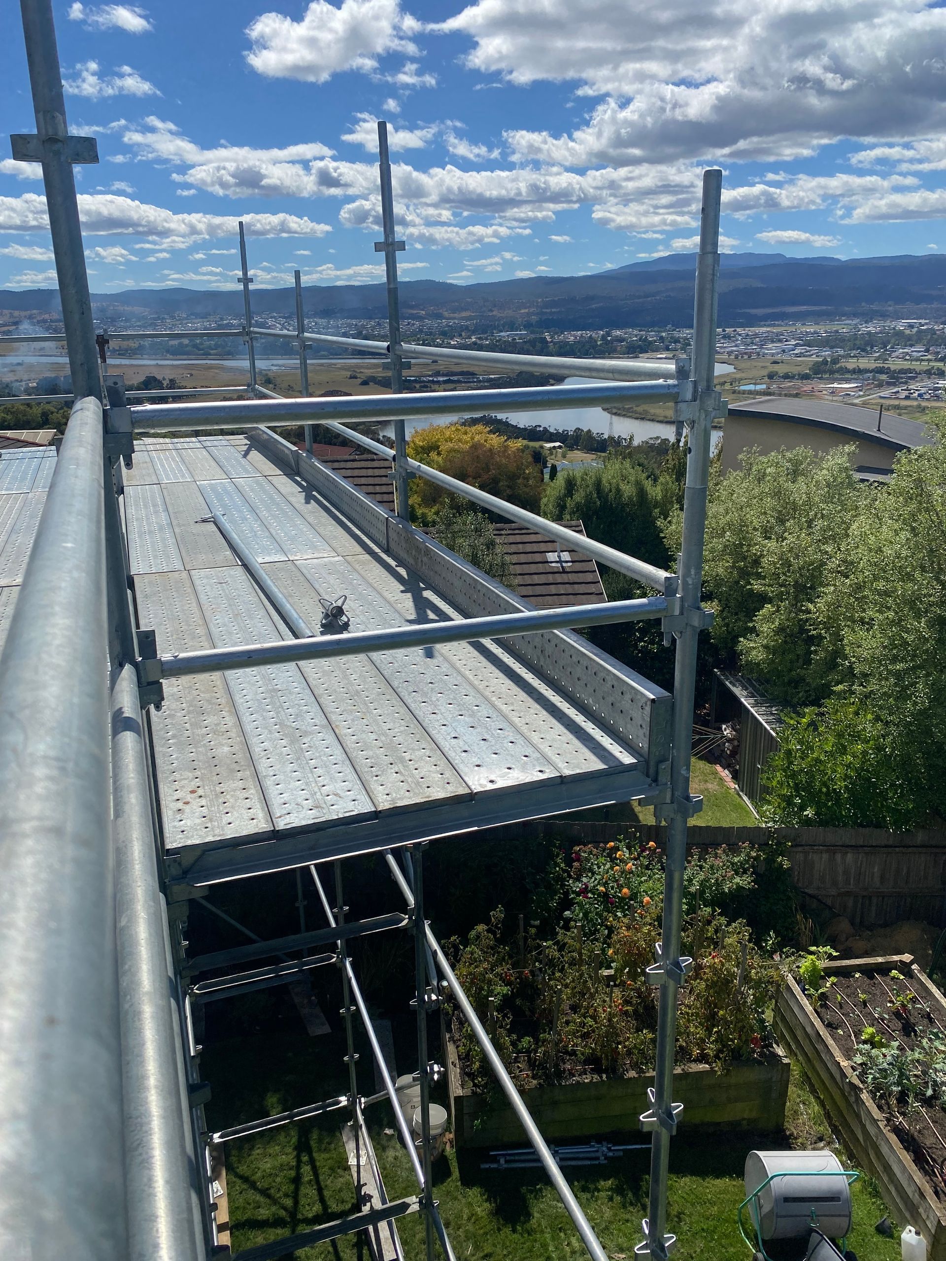 Scaffolding beside a rooftop with a city and water view under a blue sky