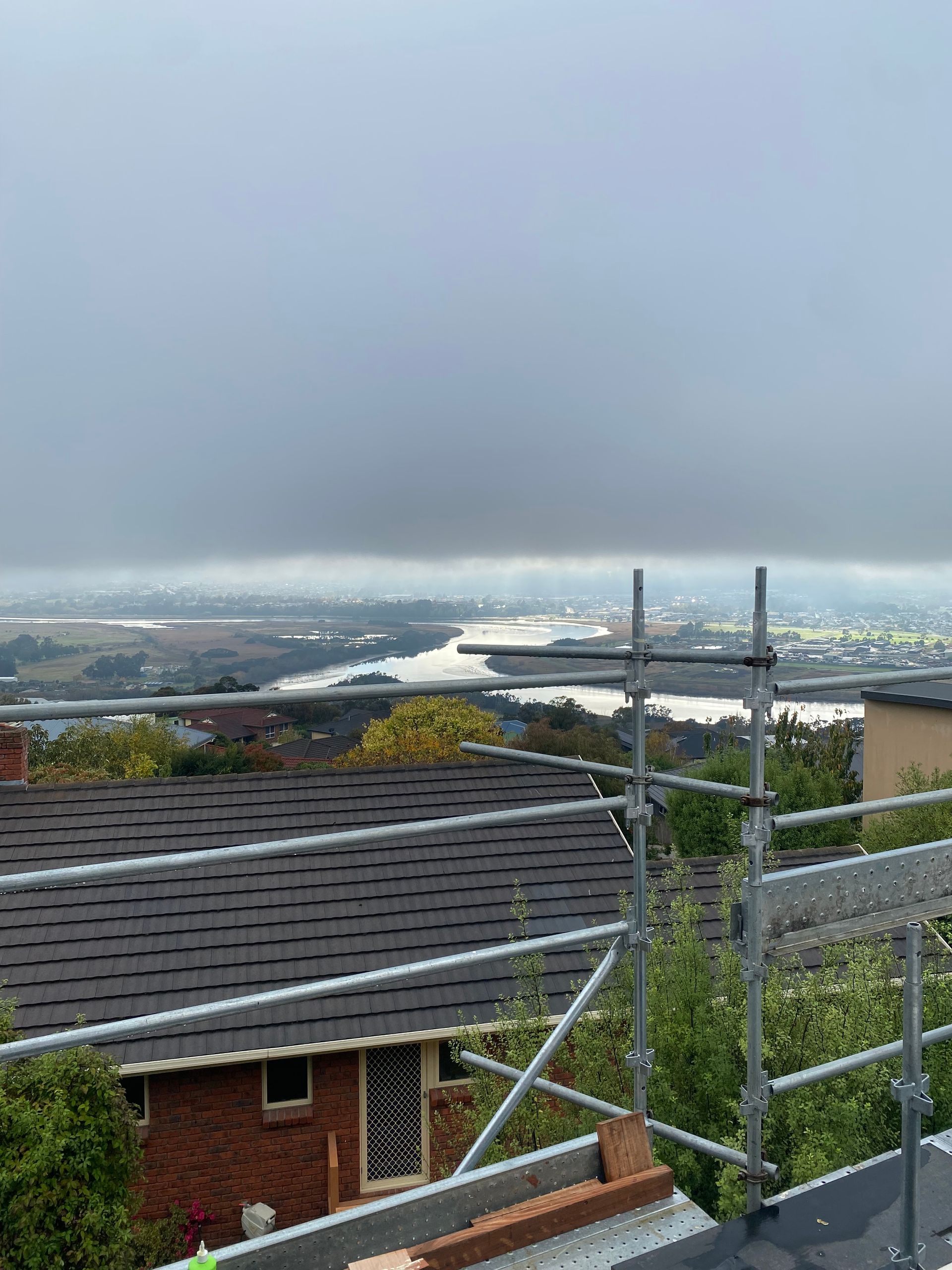 Rainy hillside view over rooftops, metal railings, and a distant city skyline under gray clouds