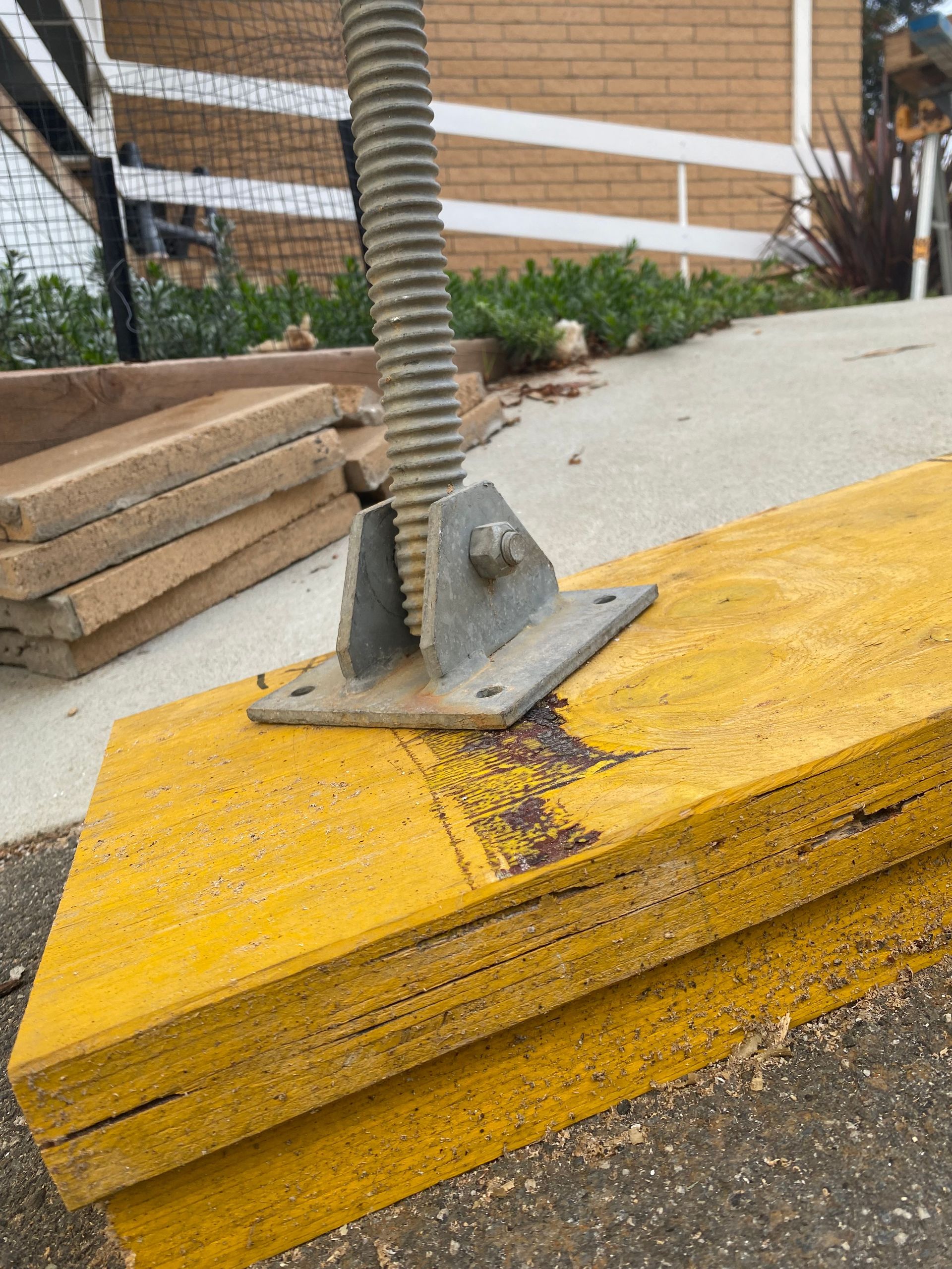 Close-up of a yellow curb ramp with a metal post base and bolts on a sidewalk outdoors