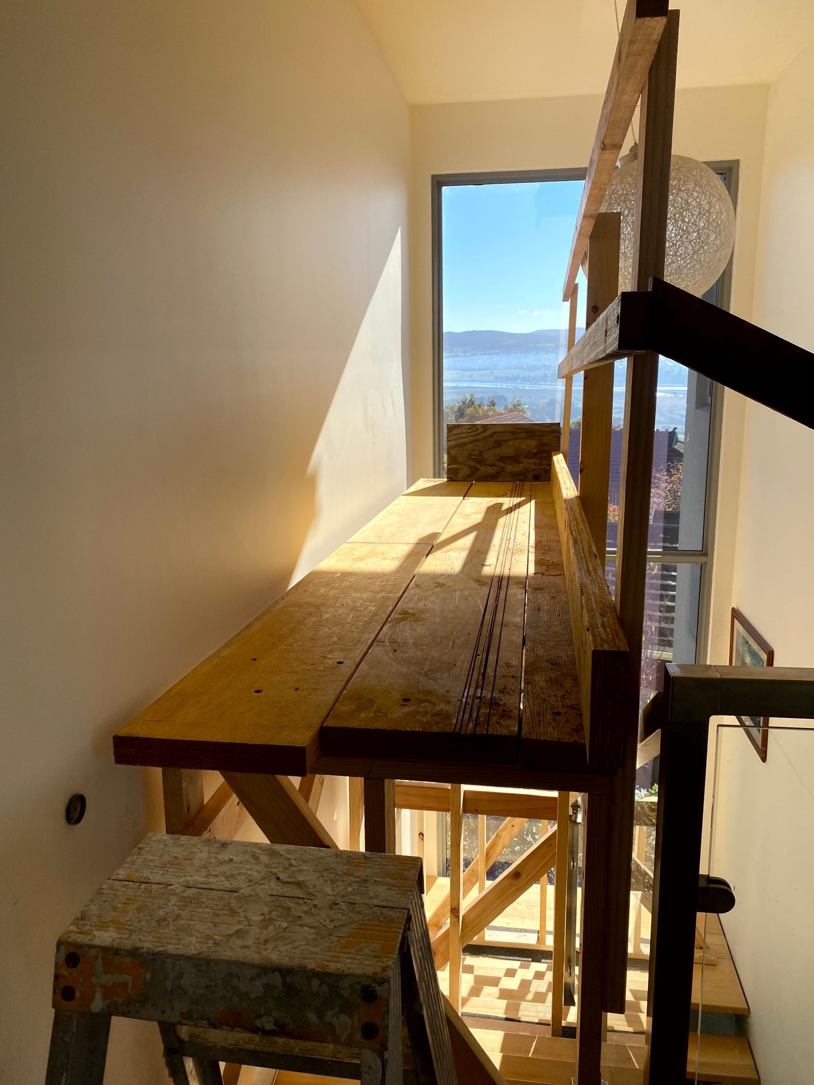 Wooden scaffolding walkway inside a narrow stairwell, lit by sunlight with a window view outside.