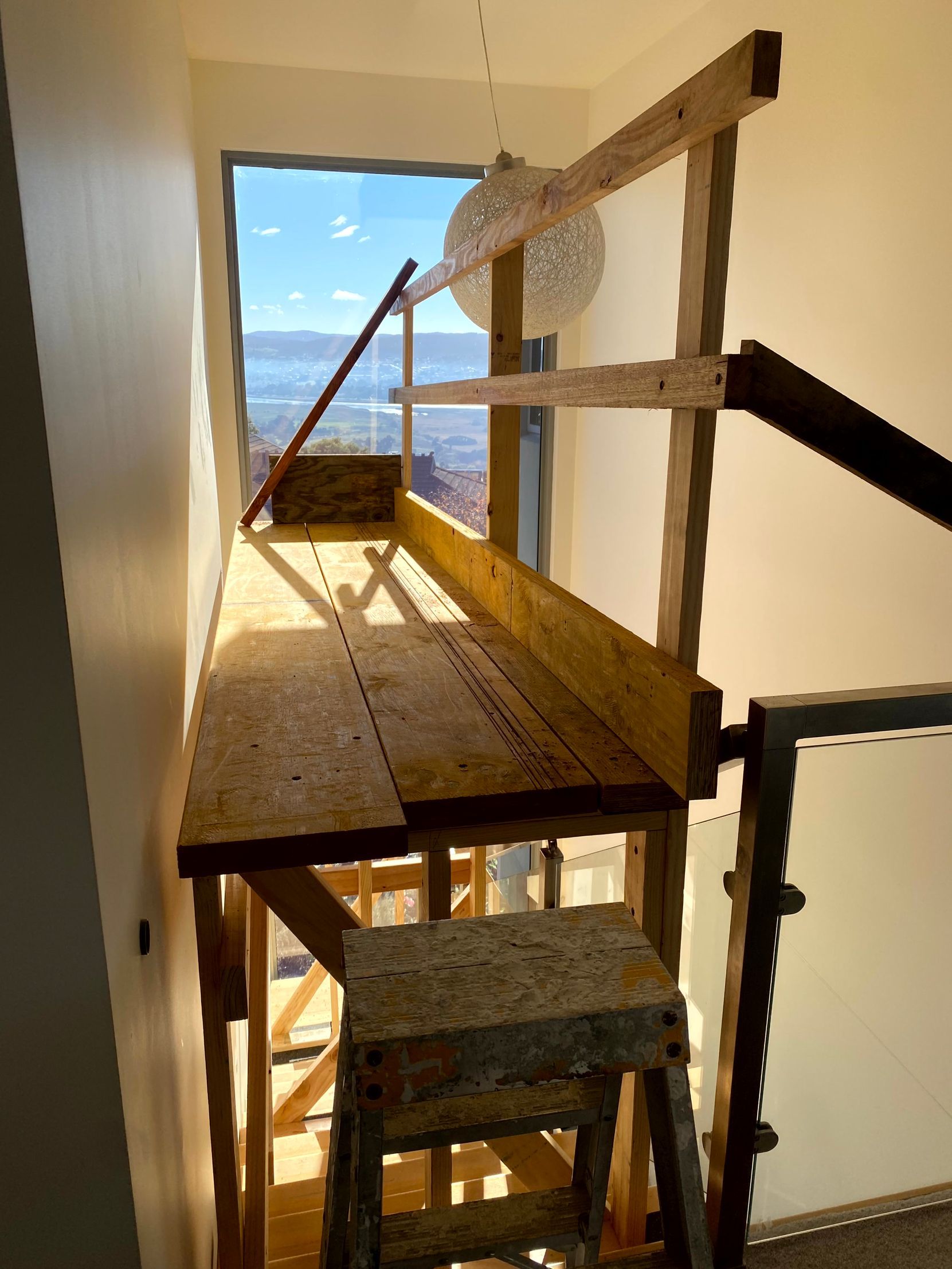 Narrow wooden stairway and platform inside a building, with ocean view through a large opening.