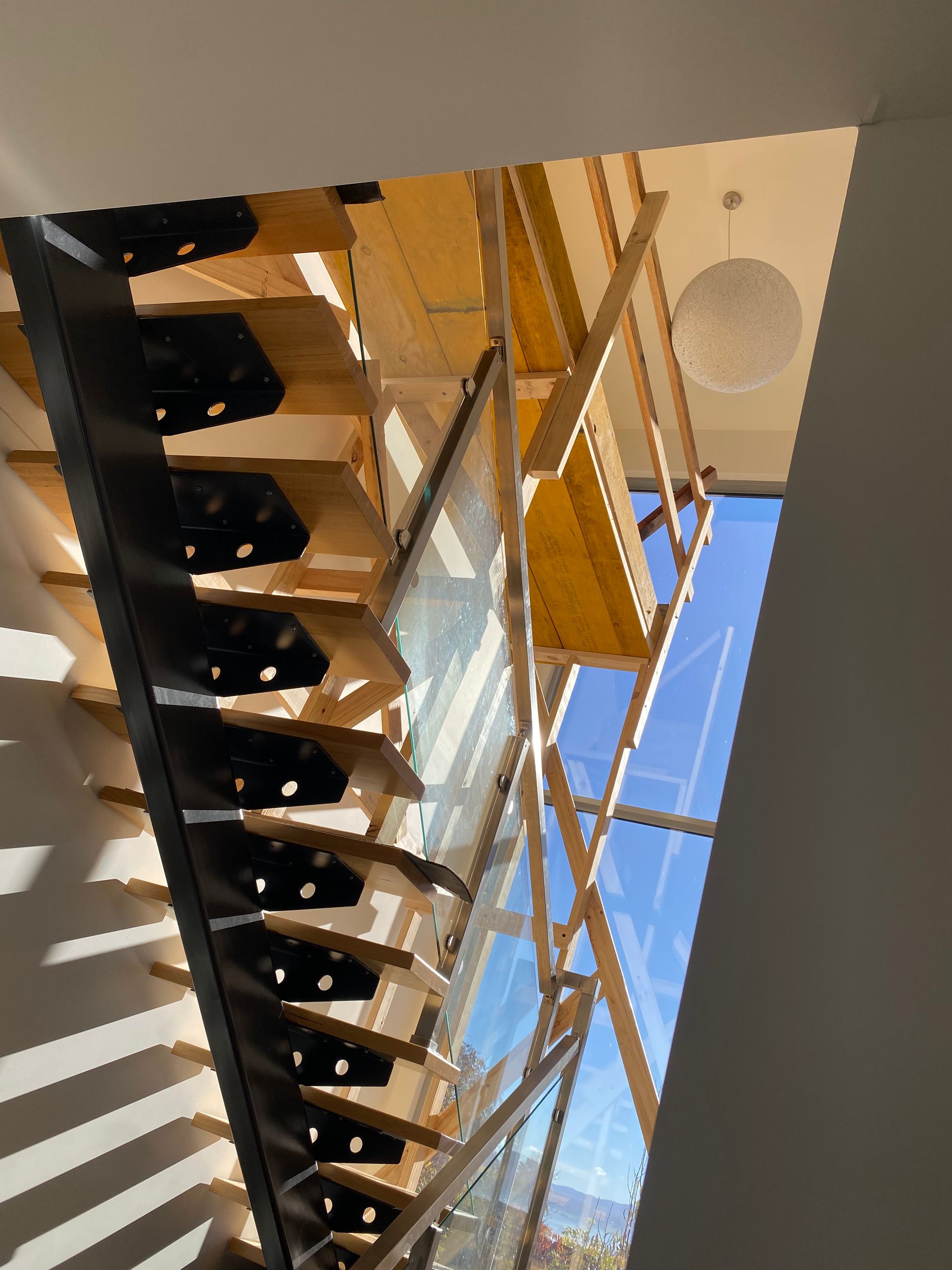 Modern staircase with wooden railings and black steps, viewed from below in a bright atrium.
