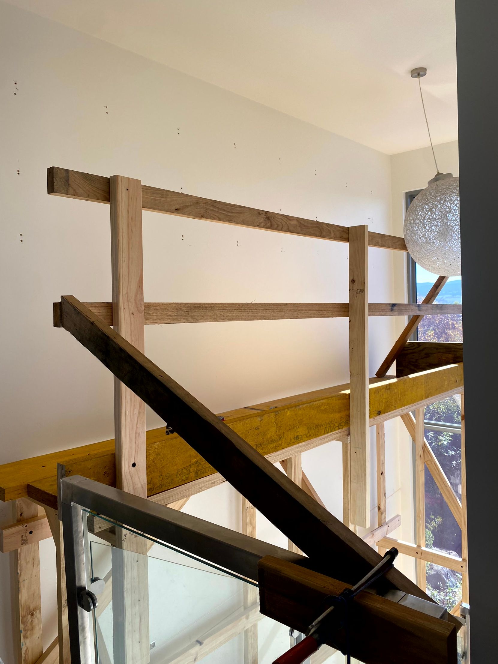 Indoor stairwell under construction with wooden railings and a dark diagonal support beam.