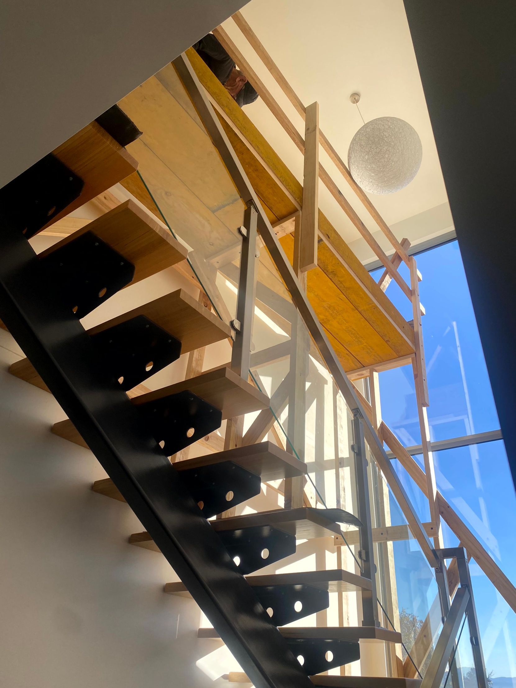 Modern indoor staircase with black steps, glass railing, and sunlight from a high window