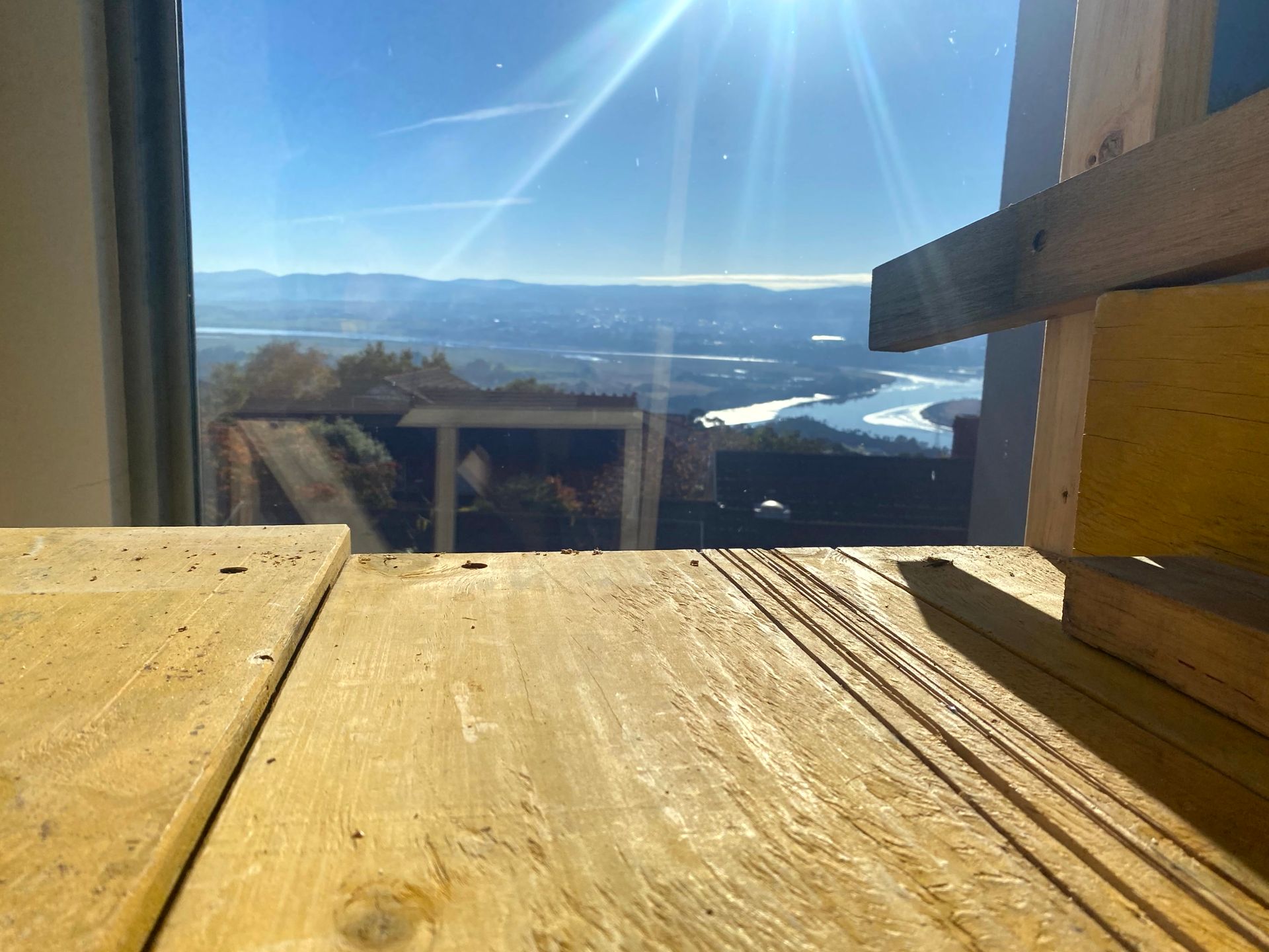 Sunlit wooden deck with mountain and water view through a window