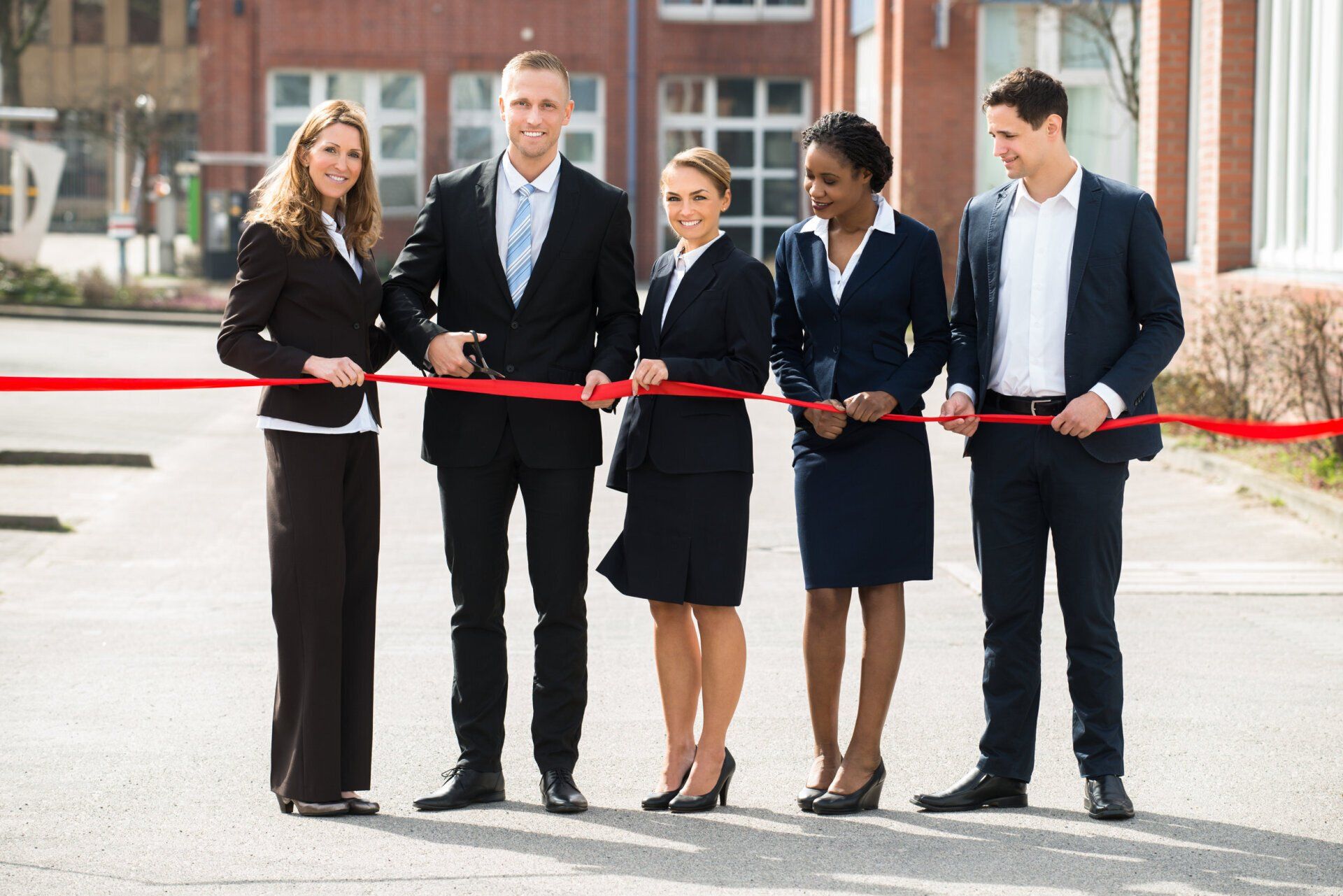 A group of business people are standing next to each other holding a red ribbon.
