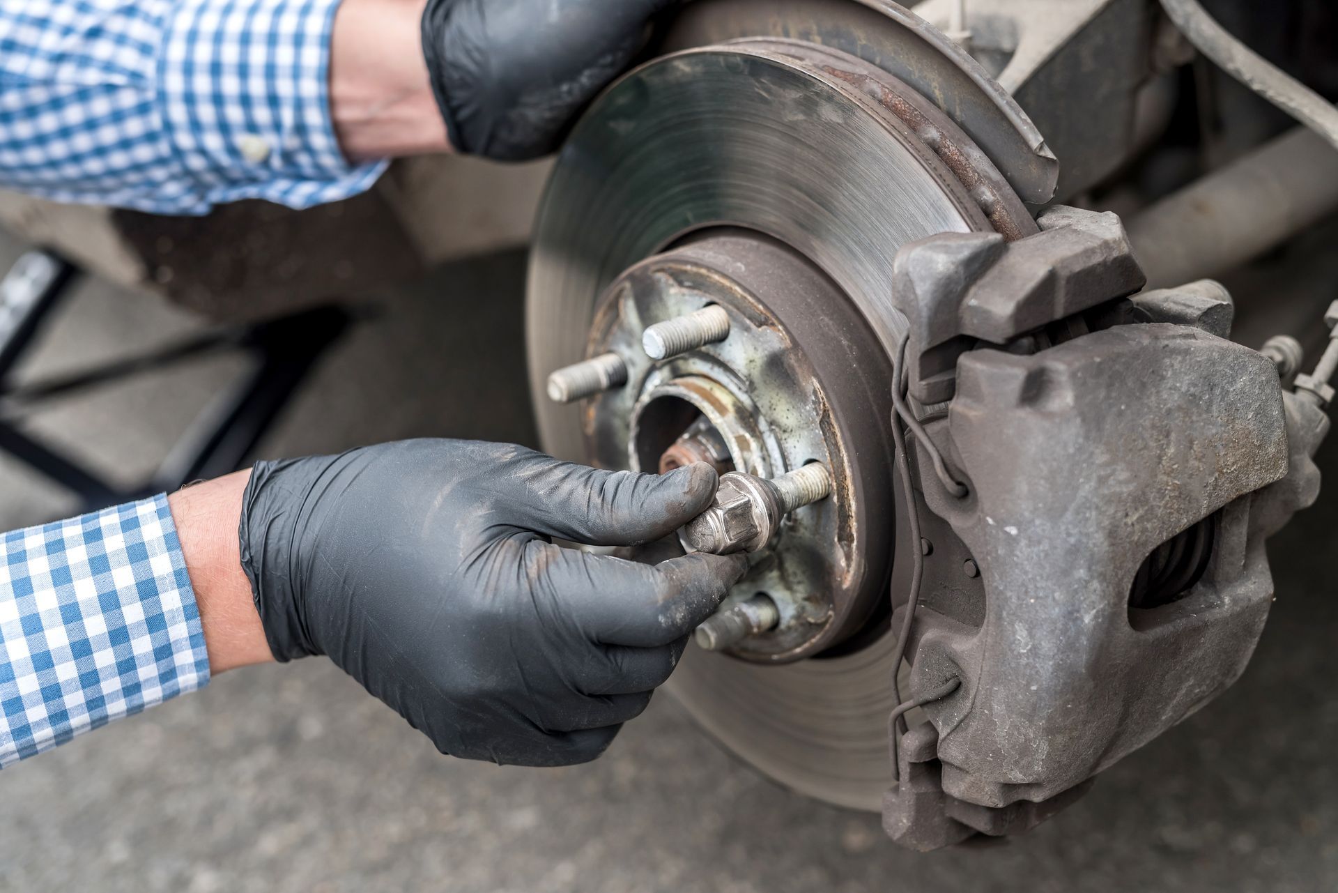 Mechanic wearing black gloves inspects a car brake rotor and caliper close-up