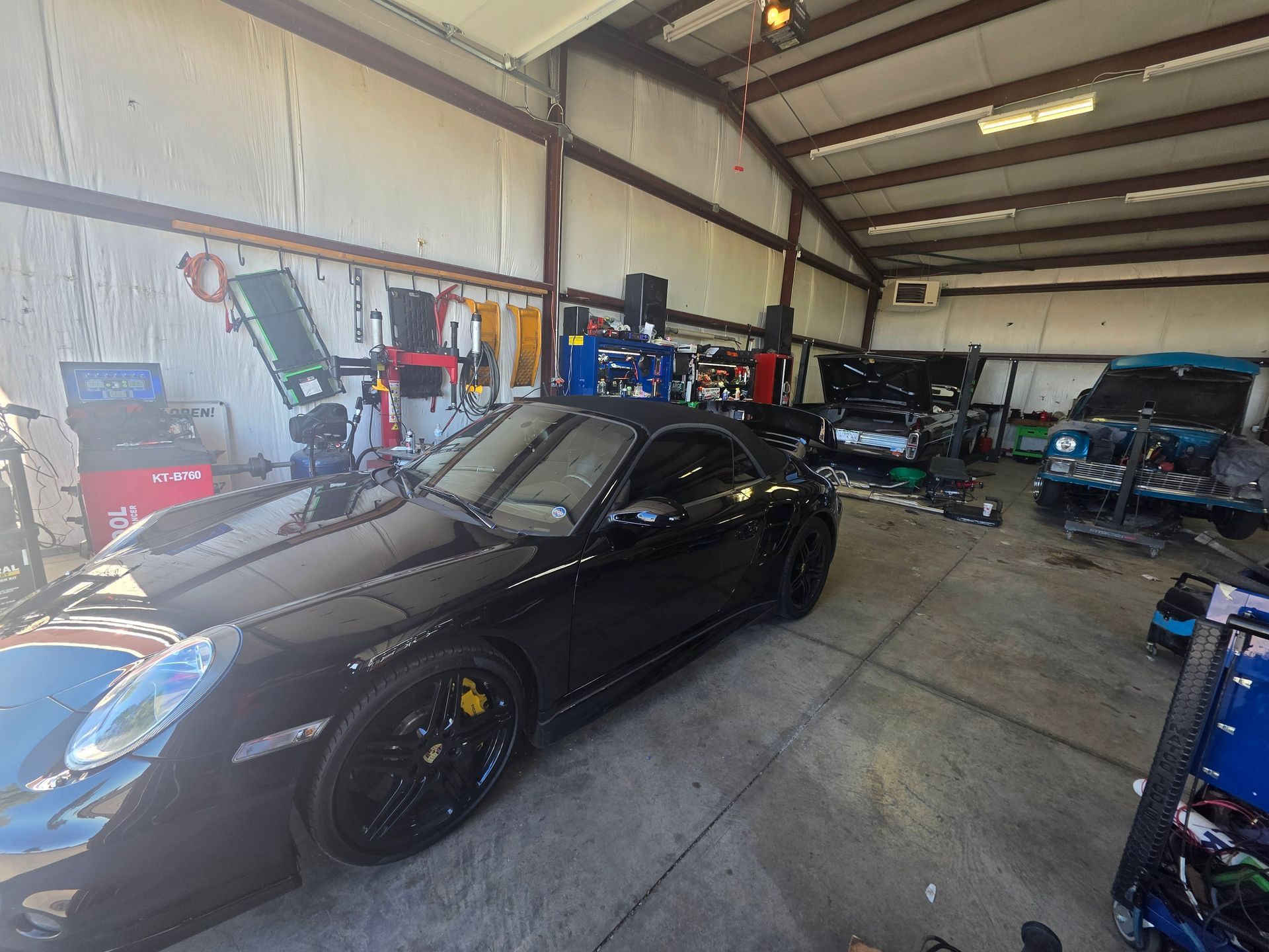 Black sports car in a garage workshop with tools and equipment around it