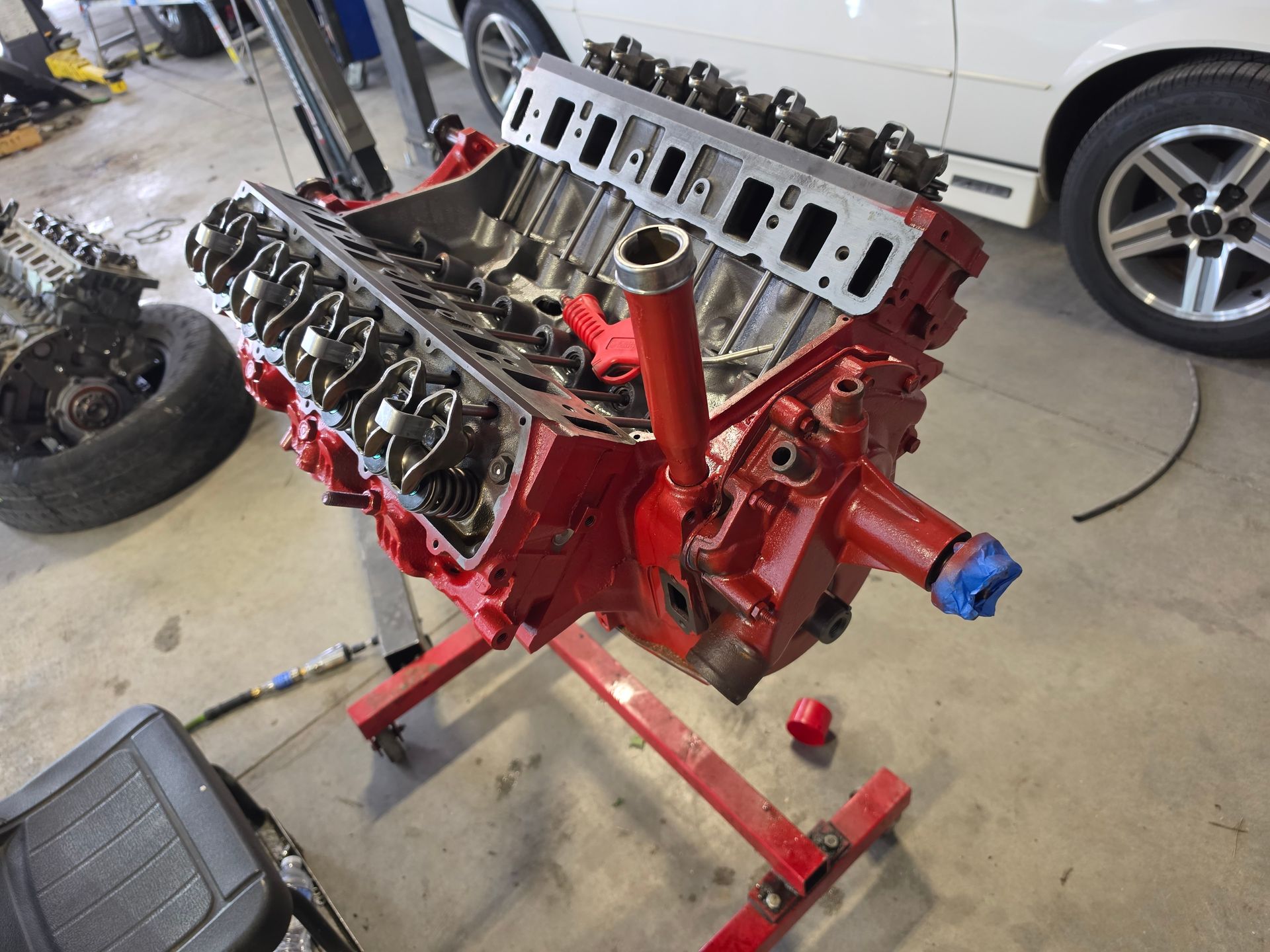 Red V8 engine block on a stand in a garage with the heads removed.