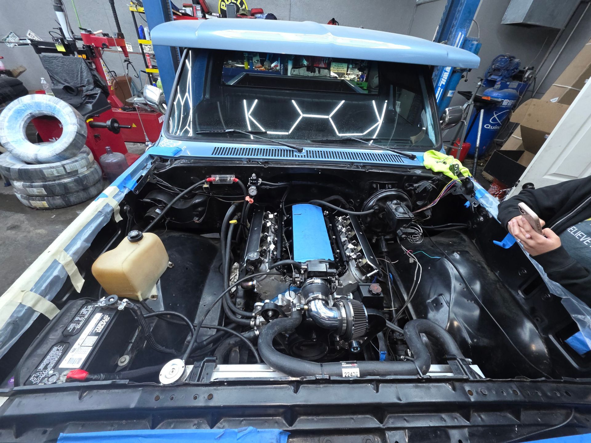 Open car engine bay with exposed turbo setup and blue intake components in a garage