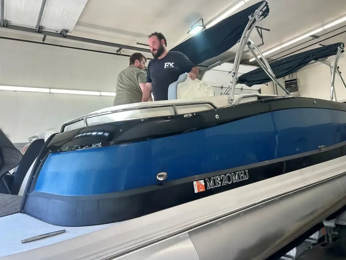Two people standing on a blue-and-white sailboat inside a garage or boathouse.
