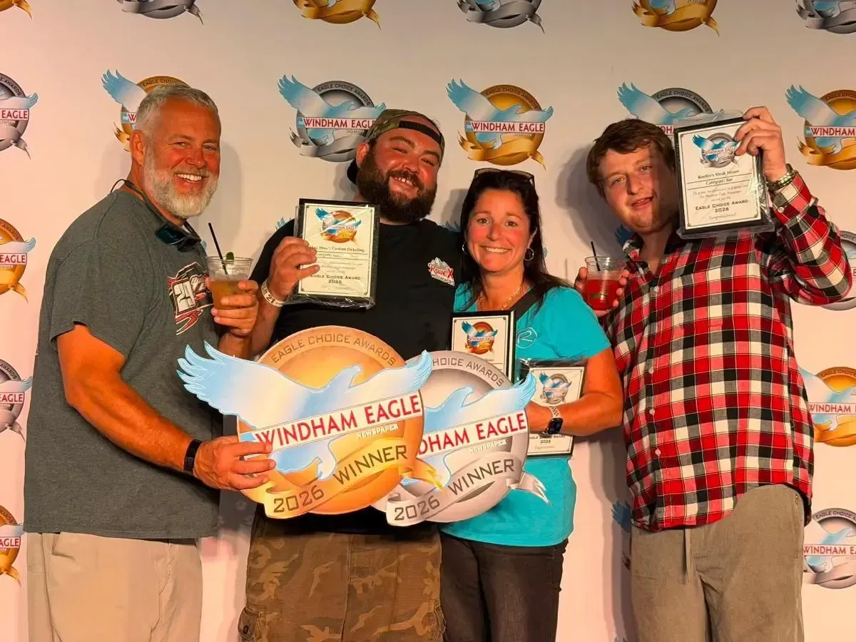 Four people posing with eagle-shaped awards and certificates at an indoor event backdrop
