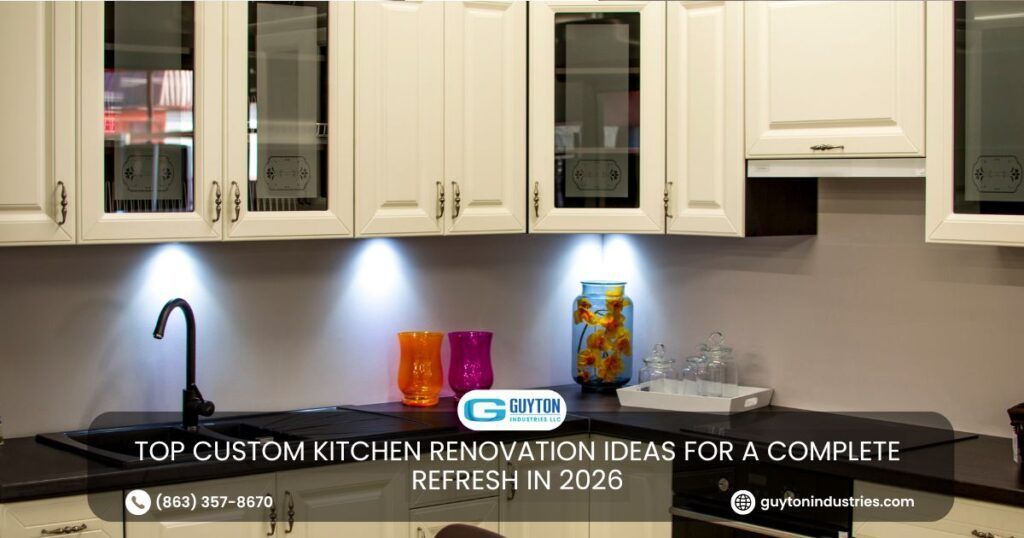 White kitchen cabinets above a dark countertop with a black faucet, under-cabinet lighting, and colorful glassware.