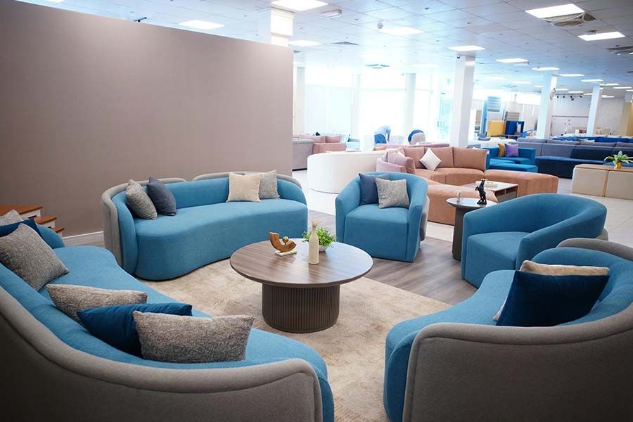 A furniture showroom features curved blue sofas and a matching armchair arranged around a round wooden coffee table.