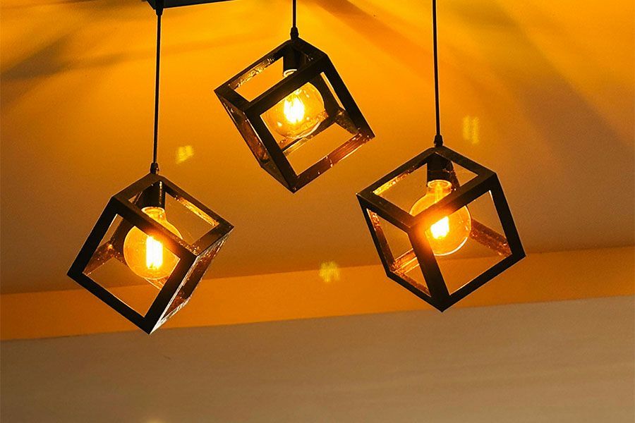 Three hanging pendant lights featuring black wire-frame cube cages and warm, glowing Edison-style bulbs.