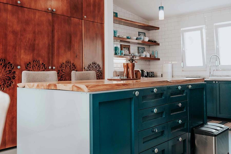 A kitchen island with a dark blue base and wooden countertop sits in front of tall, decorative wooden cabinets.