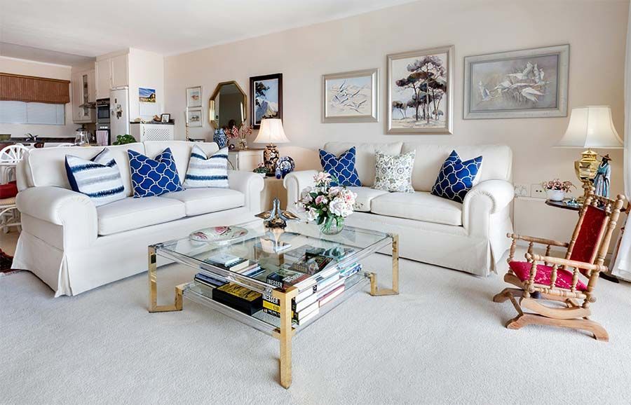 A bright, open-plan living room with two white sofas, a glass-topped coffee table, and framed art on the walls.