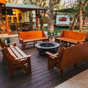 A circular fire pit surrounded by four wooden benches on a brown composite deck in a wooded outdoor seating area.