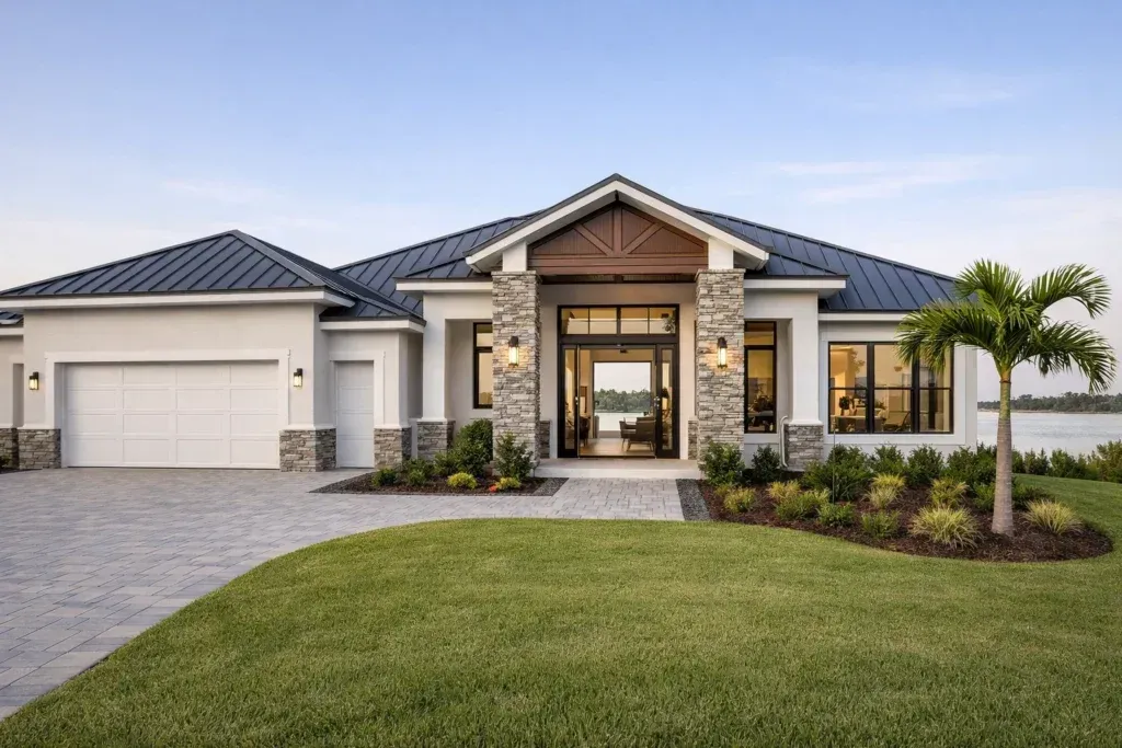 A single-story modern home with a dark metal roof, stone accents, a three-car garage, and a manicured lawn by the water.