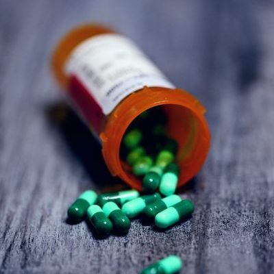 Green and blue pills are pouring out of a bottle on a wooden table.