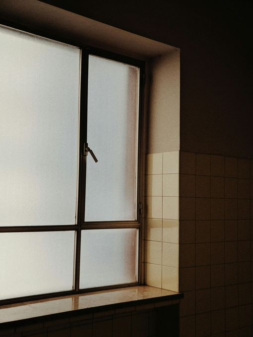 Janela com película jateada e moldura metálica, recebendo luz natural difusa, garantindo privacidade sem bloquear a iluminação.