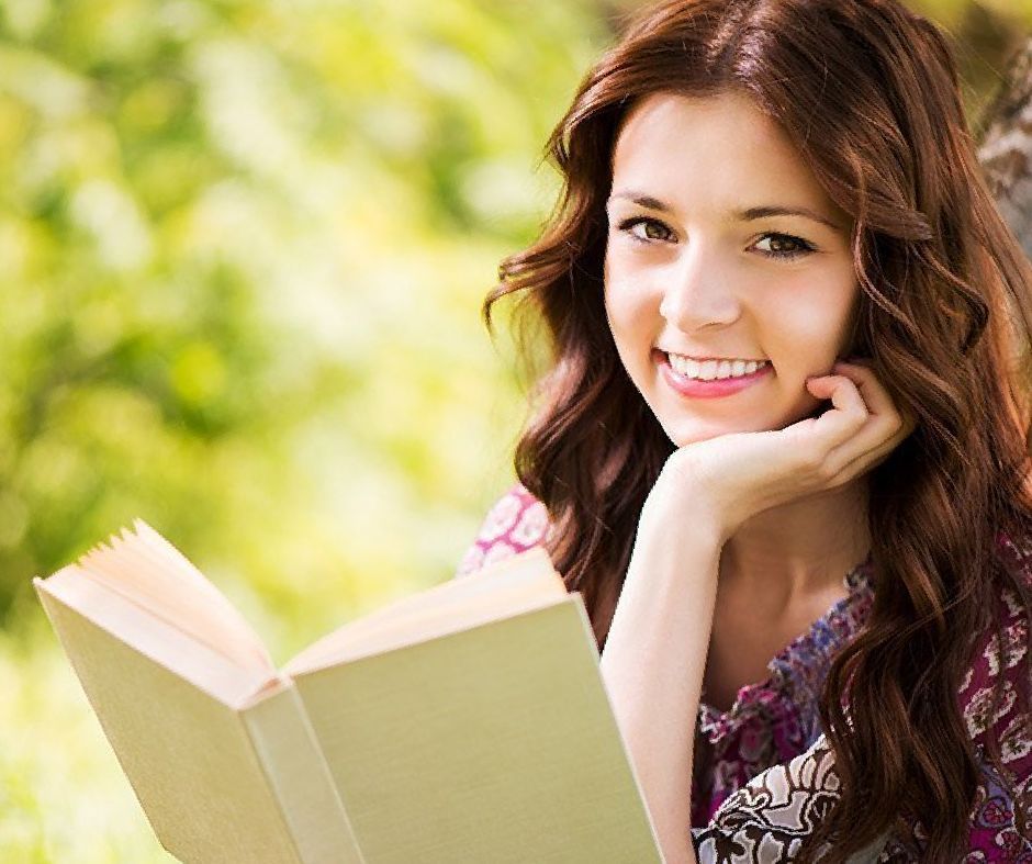 A young woman is smiling while reading a book