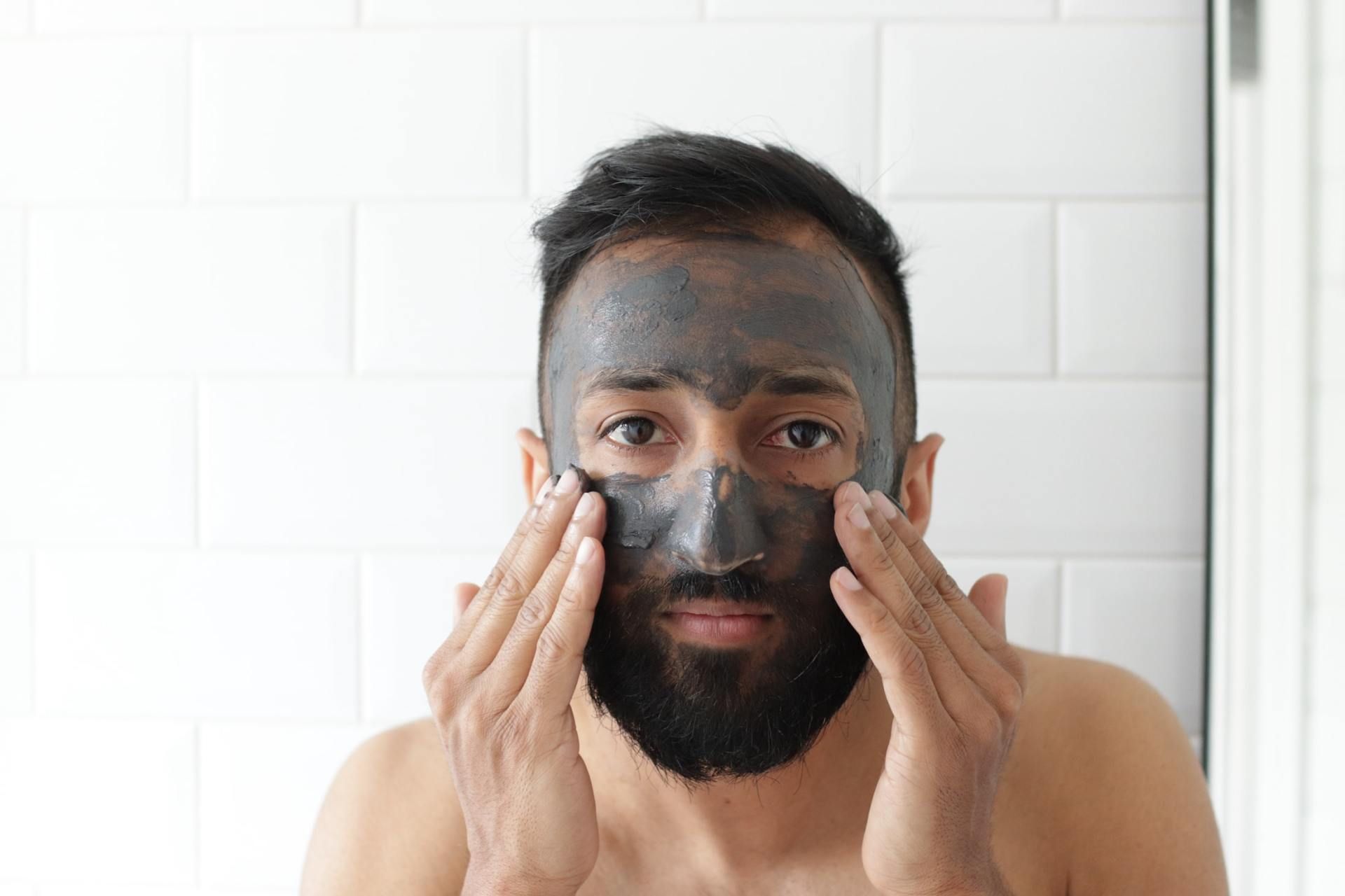 A man with a beard is applying a black mask to his face.