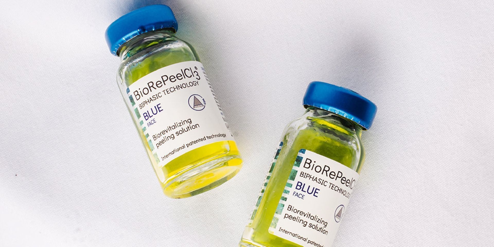 Two small bottles of yellow liquid with blue caps on a white surface.
