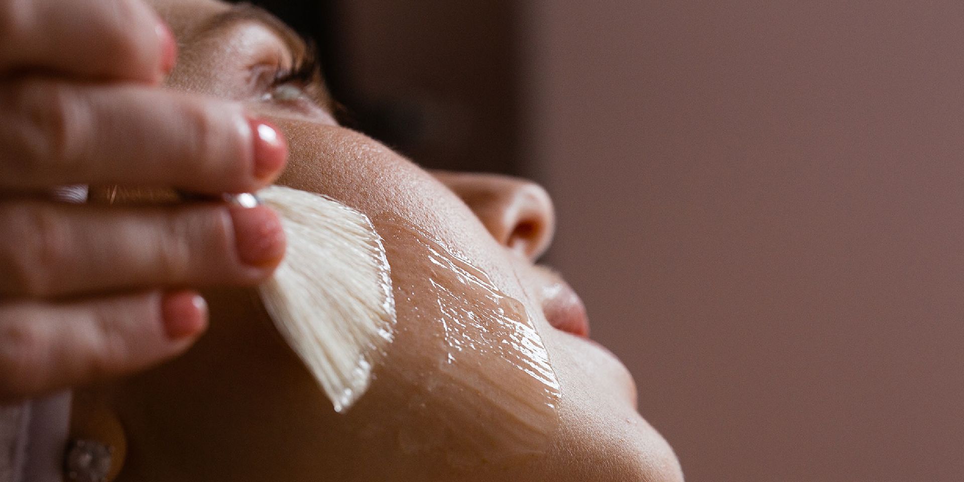 A woman is applying a cream to her face with a brush.