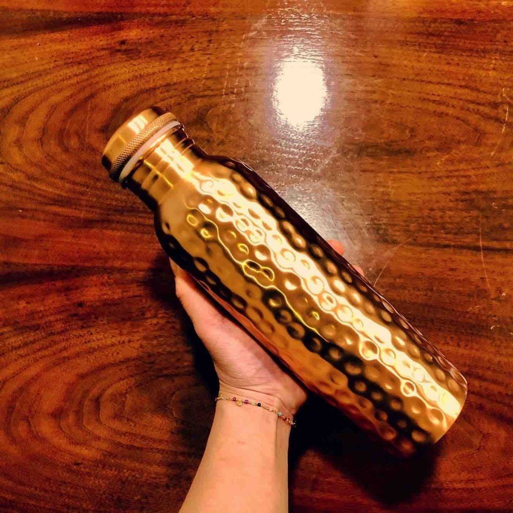 Hand holding a gold textured water bottle on a wooden table