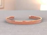 Copper open cuff bracelet on a gray surface with a blurred light background