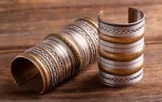 Decorative stacked metal bangles in gold, silver, and bronze on a wooden surface