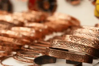 Stacked copper bracelets with engraved patterns on a white surface, warmly lit.
