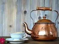Copper teapot beside a white teacup and saucer on a rustic wooden table