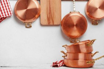 Copper pots and pans hanging on a white wall, with stacked pans and a red-and-white cloth below.