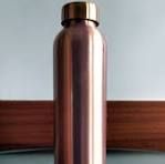 Copper-colored water bottle against a plain wall and wooden surface
