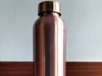 Copper-colored metal bottle with a gold cap on a wooden surface