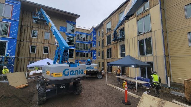 A genie lift is parked in front of a building under construction.