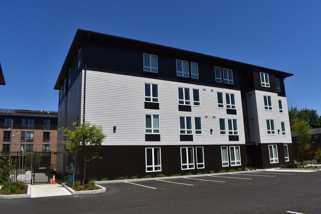 A large black and white apartment building with a parking lot in front of it.