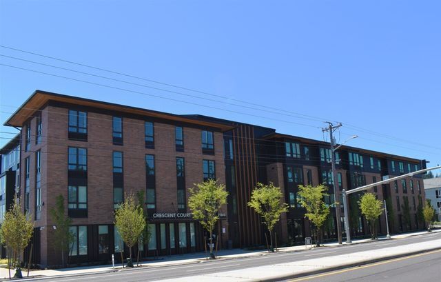 A large brick building with a lot of windows is sitting on the side of a street.