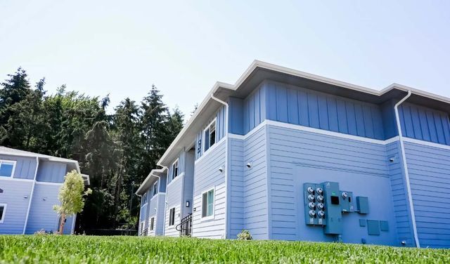 A blue and white apartment building with a lush green lawn in front of it